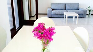 Una sala moderna con un sofá gris, una mesa de centro blanca y un jarrón de flores rosas sobre una mesa blanca.