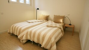 A bedroom with a bed, pillows, a bedside table, a lamp, and a window.