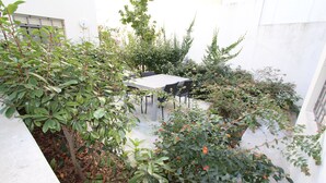 A courtyard with a table and chairs, surrounded by various plants and bushes.