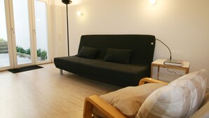 A modern room with a dark-colored sofa, a wooden chair, and a bedside table with a lamp.