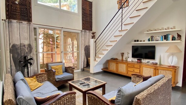 A spacious living area with wicker furniture, a glass coffee table, and a staircase leading to a balcony. - Somone: large air-conditioned villa with swimming pool, 10 people *, between Sea and Lagoon (Unknown)