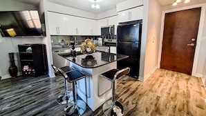 A modern kitchen with a central island, stainless steel appliances, and a flat-screen TV mounted on the wall. - 2-Bed, 2-Bath Condo w/Pool & Parking by Square 1 (Mississauga)