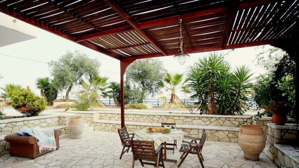 An outdoor patio with stone flooring, a wooden table with chairs, and a pergola overhead. - Olga Luxury Apt Lower ( Adults only) (Paxoi)