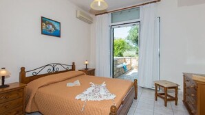 A bedroom with a bed, bedside tables, a dresser, a painting, and a view through a glass door to an outdoor area. - Olga Luxury Apt Lower ( Adults only) (Paxoi)