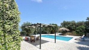A pool area with a pergola, lounge chairs, and a table with chairs. - Olga Luxury Apt Lower ( Adults only) (Paxoi)
