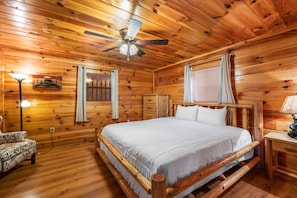 Cozy bedroom with a large bed, ceiling fan, and wooden walls.