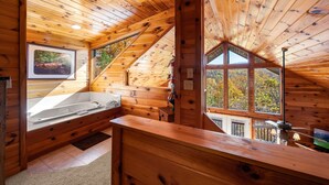 A cabin with a wooden interior, a large window, a bathtub, and a view of trees. - Breathtaking Mtn VIEWS!! Cozy yet spacious peaceful cabin in the mountains! (Sevierville)