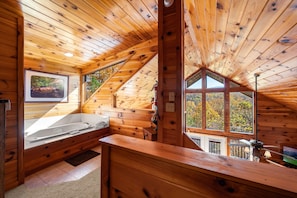 Cozy cabin-style room with a sloped ceiling and large window offering a view of the surrounding trees.