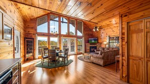 A wooden cabin interior with a dining area, living room, and large windows offering views. - Breathtaking Mtn VIEWS!! Cozy yet spacious peaceful cabin in the mountains! (Sevierville)