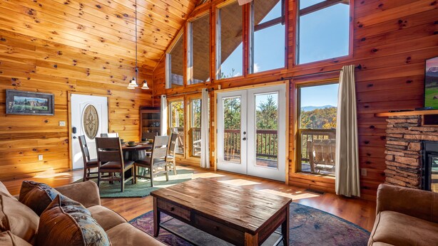 A spacious wooden cabin with a large dining area, a fireplace, and large windows offering a view of the outdoors. - Breathtaking Mtn VIEWS!! Cozy yet spacious peaceful cabin in the mountains! (Sevierville)