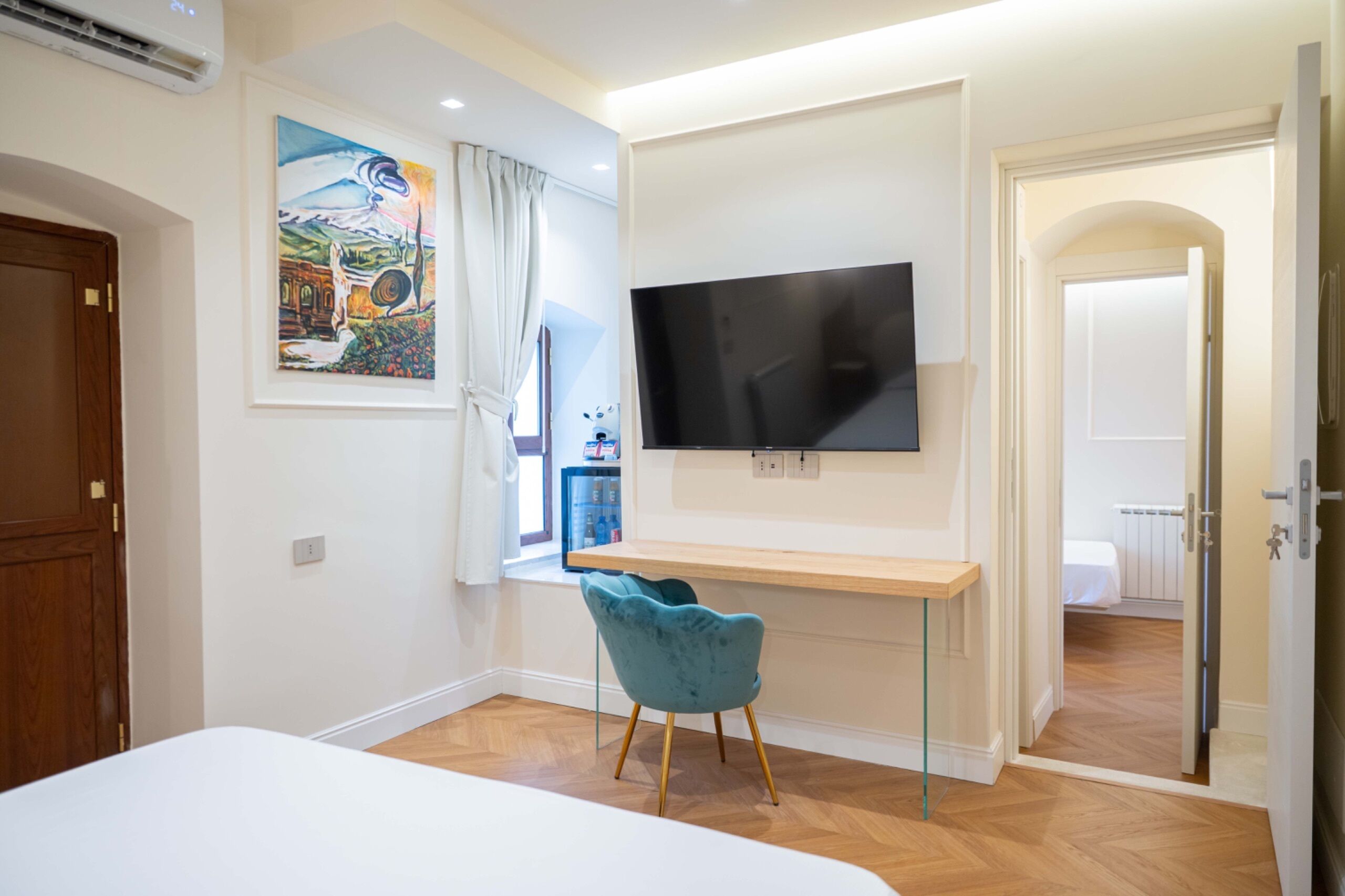 Een slaapkamer met een bed, een bureau, een televisie, een stoel en een schilderij aan de muur.