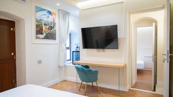 Een slaapkamer met een bed, een bureau, een televisie, een stoel en een schilderij aan de muur.