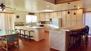 Una cocina moderna con armarios de madera, una isla central con taburetes, un comedor con mesa y sillas, y un ventilador de techo.
