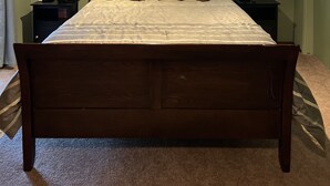 Un dormitorio con una cama de madera, dos mesitas de noche, un ventilador de techo y dos ventanas con persianas.