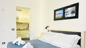 Et hotelværelse med seng, lille skrivebord, tv ophængt på væggen og udsigt til køkkenet.