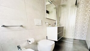 Et moderne badeværelse med bidét, toilet og et underskab med spejl.