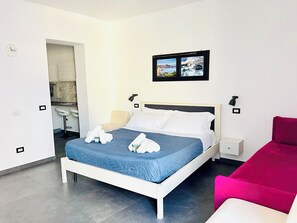 Habitació d'hotel amb llit, una vetusta, una cadira vermella i un bany visible a través d'una porta oberta.