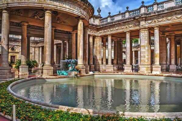 A grand courtyard with a central fountain, surrounded by classical columns and ornate balustrades.
