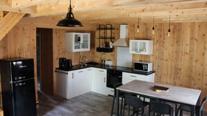 Kompakti keittiö, jossa on jääkaappi, mikroaaltouuni ja liesi. Keittiössä on ruokapöytä tuoleineen sekä riippuvalaisin.