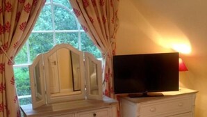 A bedroom with a vanity, a television on a dresser, and a window with curtains. - Chalkcroft lodge (Andover)