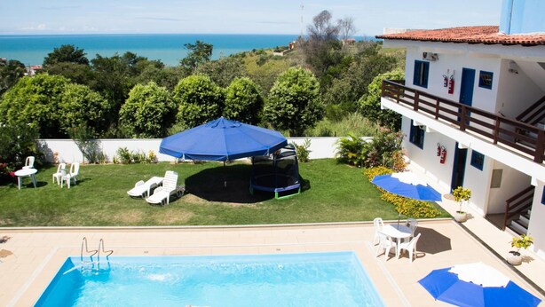 Un área de piscina con vista al mar, mobiliario exterior y un edificio con balcón.