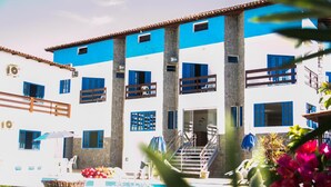 Un edificio con fachada azul y blanca, varios balcones y una zona de piscina con mobiliario exterior.