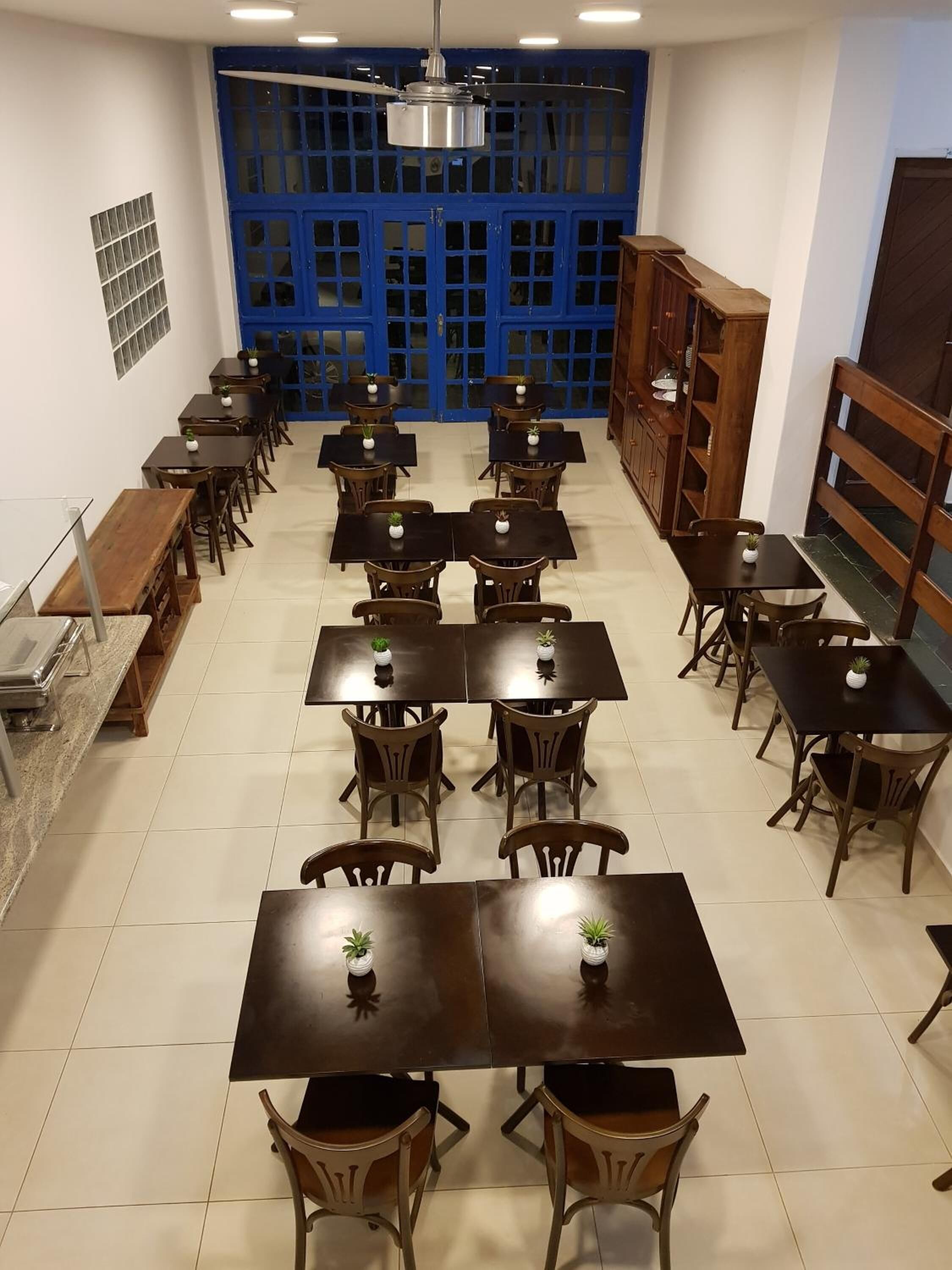 Un'ampia sala da pranzo con diversi tavoli e sedie, una ventola a soffitto e una porta blu sullo sfondo.