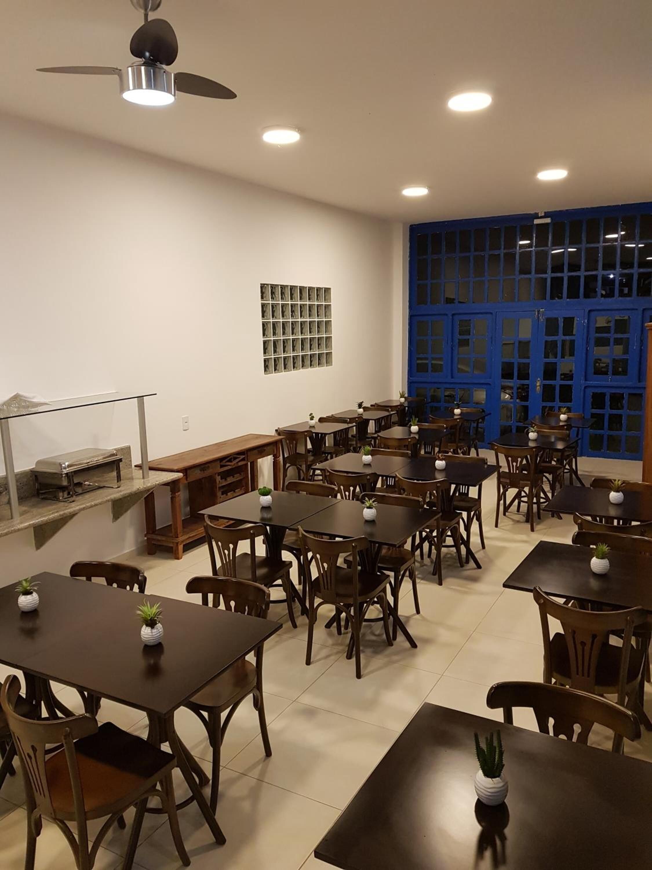 Un vaste espace de salle à manger avec plusieurs tables et chaises, un ventilateur de plafond, un éclairage encastré et une porte bleue dotée de panneaux de verre.