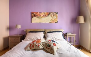 Un dormitorio con una cama, dos mesitas de noche, una lámpara y un cuadro en la pared.