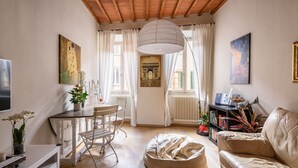 Una sala de estar acogedora con techo de madera, una mesa de comedor con sillas, un sofá, un sillón tipo pera y una estantería.