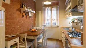 Una cocina compacta con pared de ladrillo, muebles blancos, una mesa de madera y una estufa a gas.