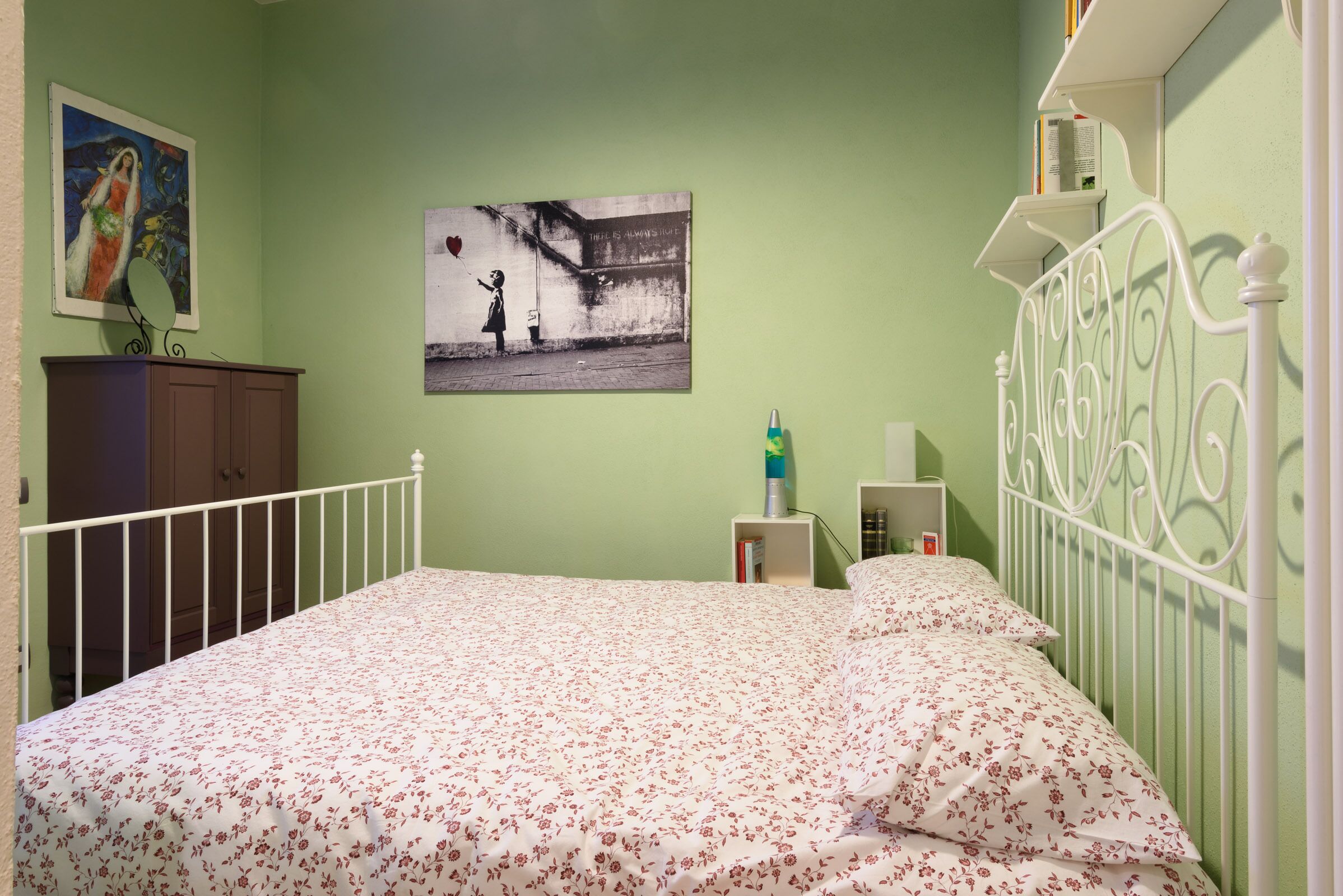 Un dormitorio con cama, cómoda, mesita de noche y una pared con dos cuadros.