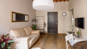 Una sala de estar con un sofá color crema, una mesa blanca, un televisor y una lámpara en el techo.