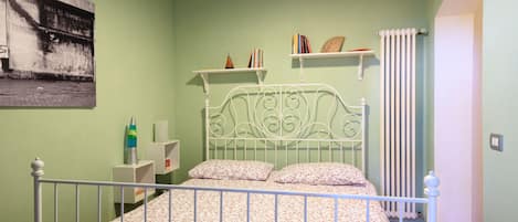 A bedroom with a bed, a radiator, and shelves with books and decorative items.