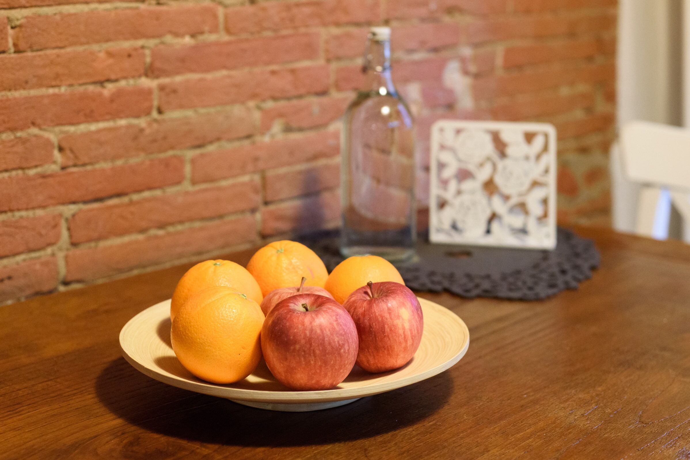 A wooden table with a plate of fruit, a glass bottle, and a decorative item.