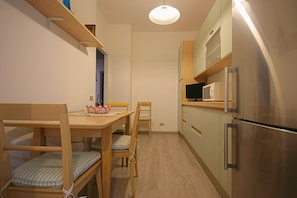A compact kitchen with a dining table, chairs, a refrigerator, and a microwave.