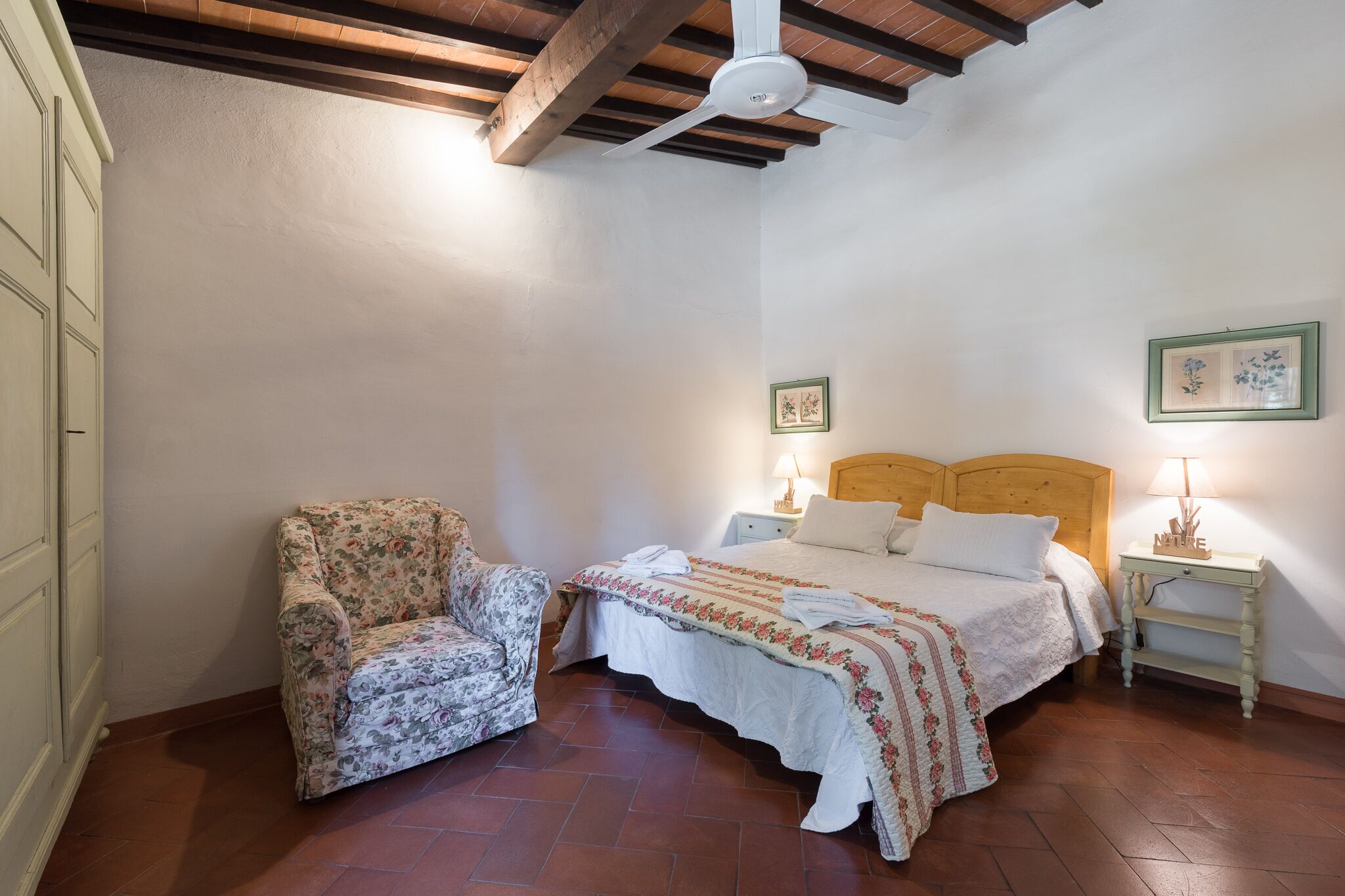 Une chambre à coucher avec un lit, une chaise, une table de chevet et deux tableaux encadrés au mur.