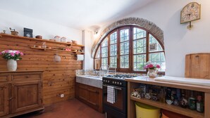 A rustic kitchen with wooden cabinetry, a stove, and a large arched window.