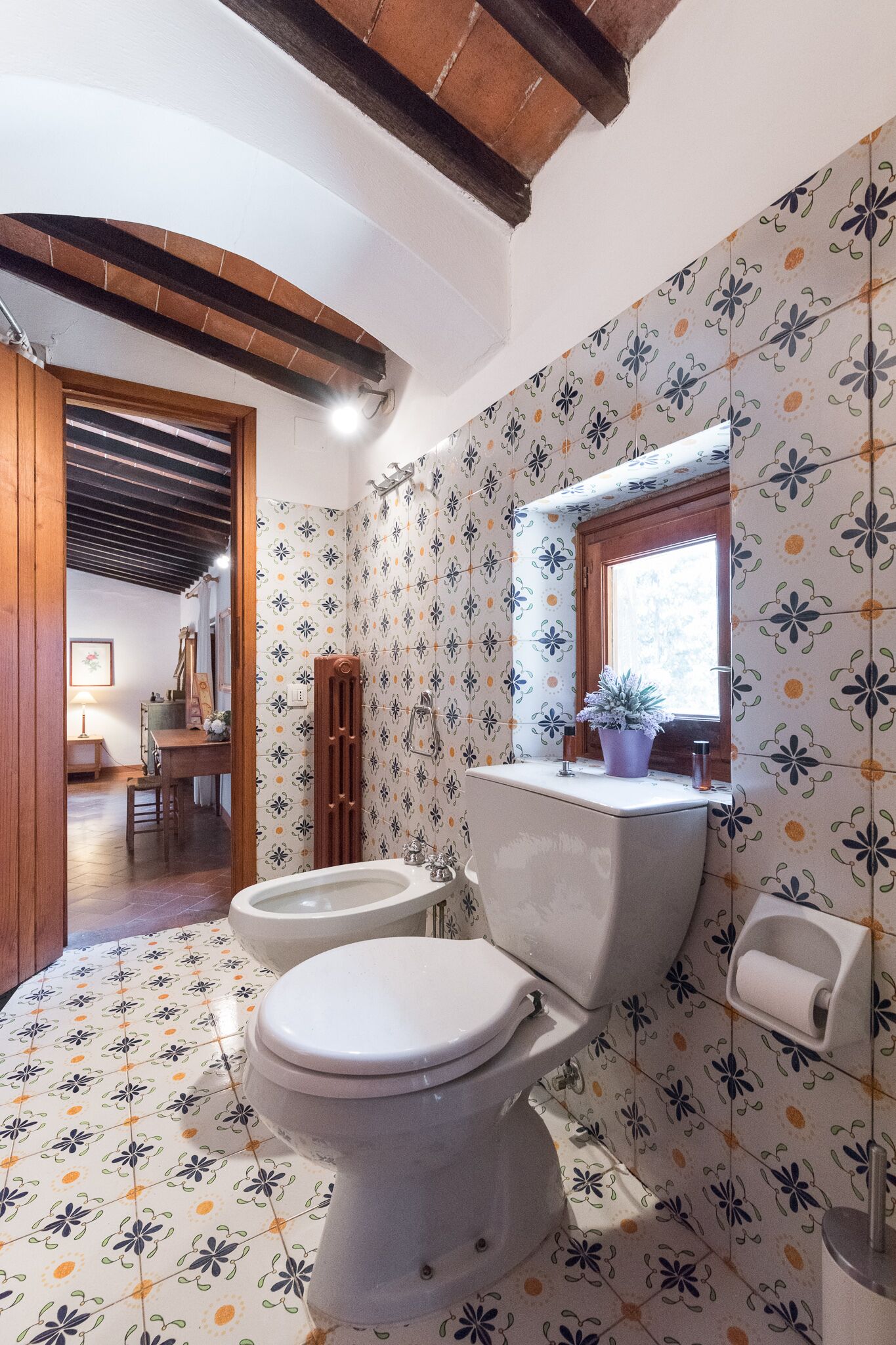 Ein Badezimmer mit Toilette, Bidet und einem Fenster mit Blumentopf.