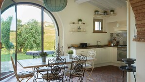 Een keuken met een eethoek, met een groot raam, witte kasten en decoratieve objecten op planken.