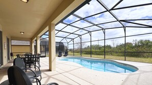 A covered outdoor area with a pool, chairs, and a grill.
