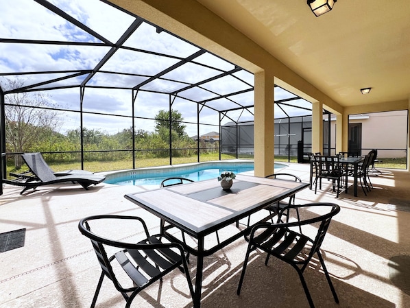 Un espacio al aire libre techado con piscina, asientos y una mesa.