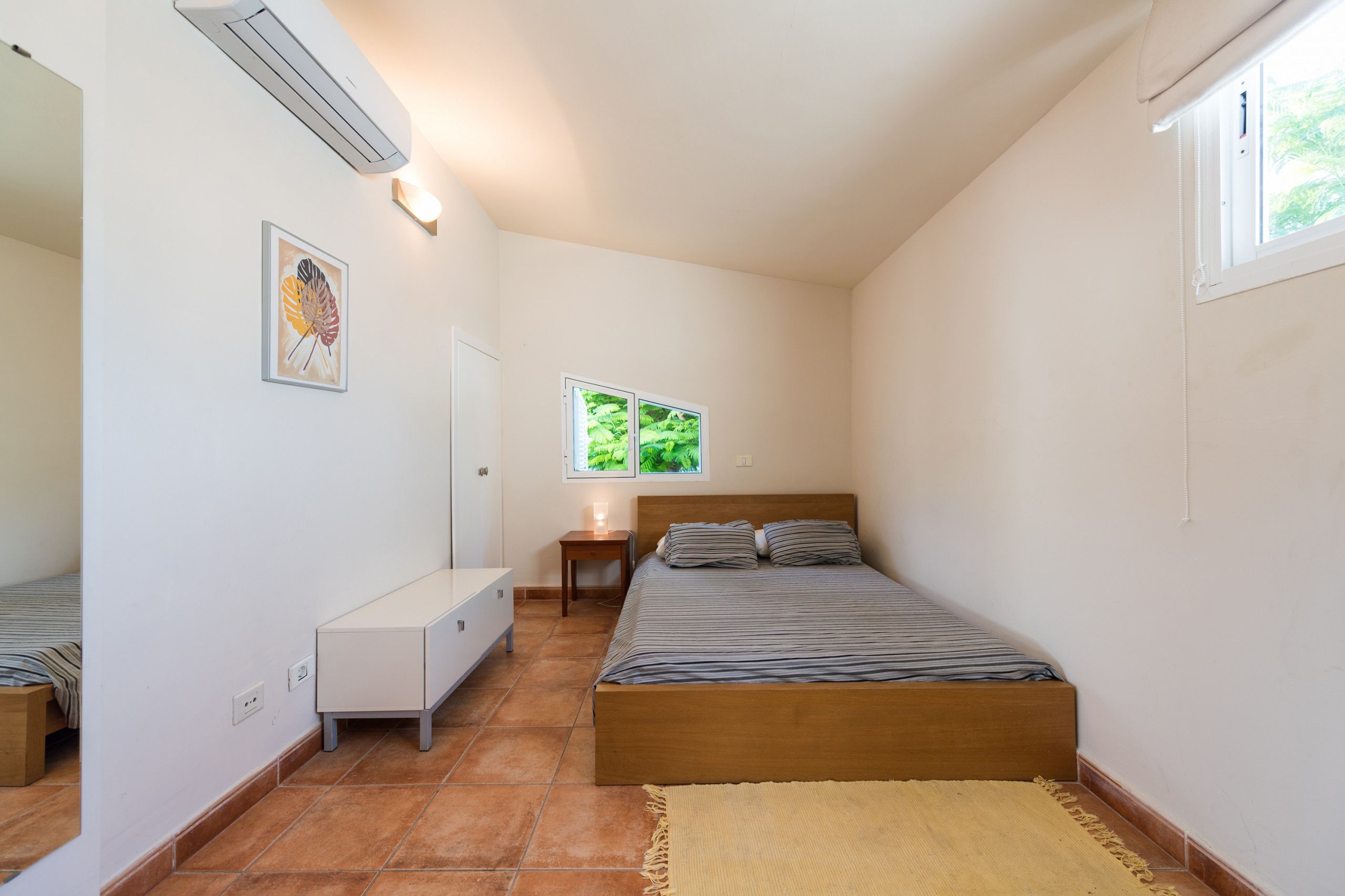 Ein Schlafzimmer mit Bett, Nachttisch und einem Fenster mit Blick auf Grünflächen.
