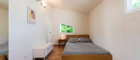 Ein Schlafzimmer mit Bett, Nachttisch und einem Fenster mit Blick auf Grünflächen.