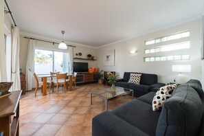 A living room with a sofa, a coffee table, a TV, and a dining area with chairs and a table.
