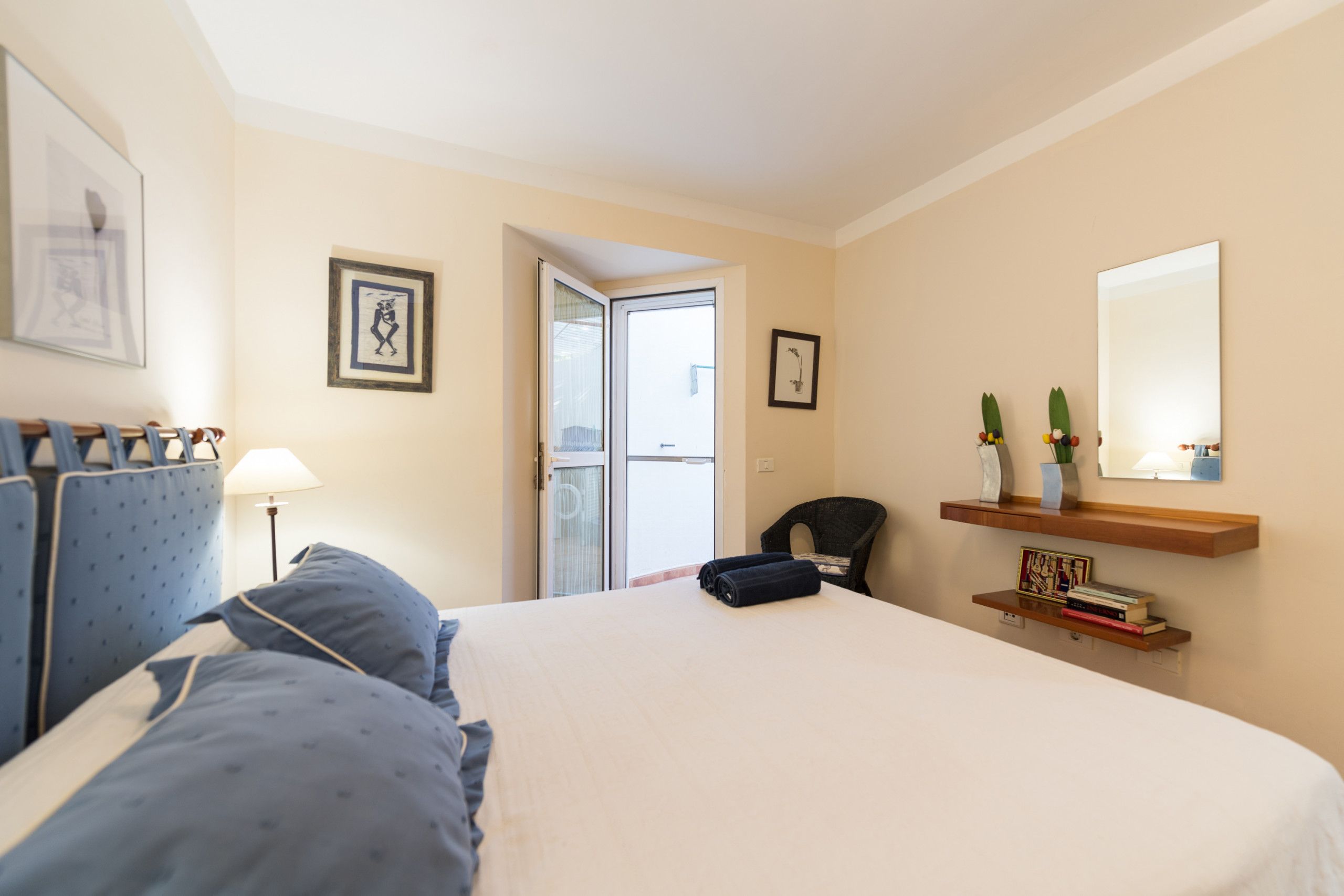 Quarto de hotel com cama, cadeira, escrivaninha, janela e porta.