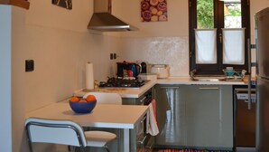 A compact kitchen with a central island, a dining area with a chair, and a large window with curtains. - Relaxing House surrounded by Olive trees, wonderful sea view (Dolcedo)