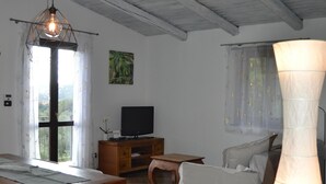 A spacious living area with a wooden dining table, white chairs, a sofa, and a television. - Relaxing House surrounded by Olive trees, wonderful sea view (Dolcedo)