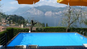 A swimming pool with yellow umbrellas, a view of a lake, and mountains in the background.