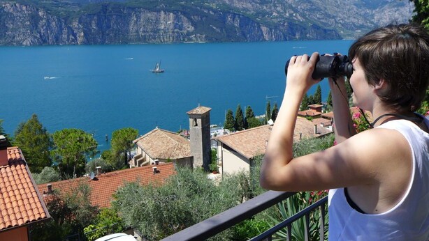 A person taking a photograph of a lake with mountains in the background.